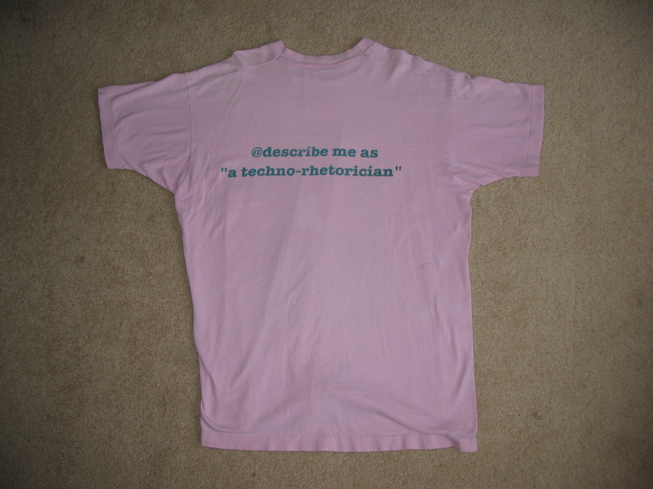 The first CWC tee shirt, in pink, from the Columbia, Missouri conference in 1994. Text reads @describe me as a technorhetorician