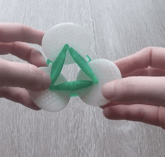 A gif of two hands playing with a 3D printed, plastic spatial manipulation toy comprised of green and white interlocking discs.