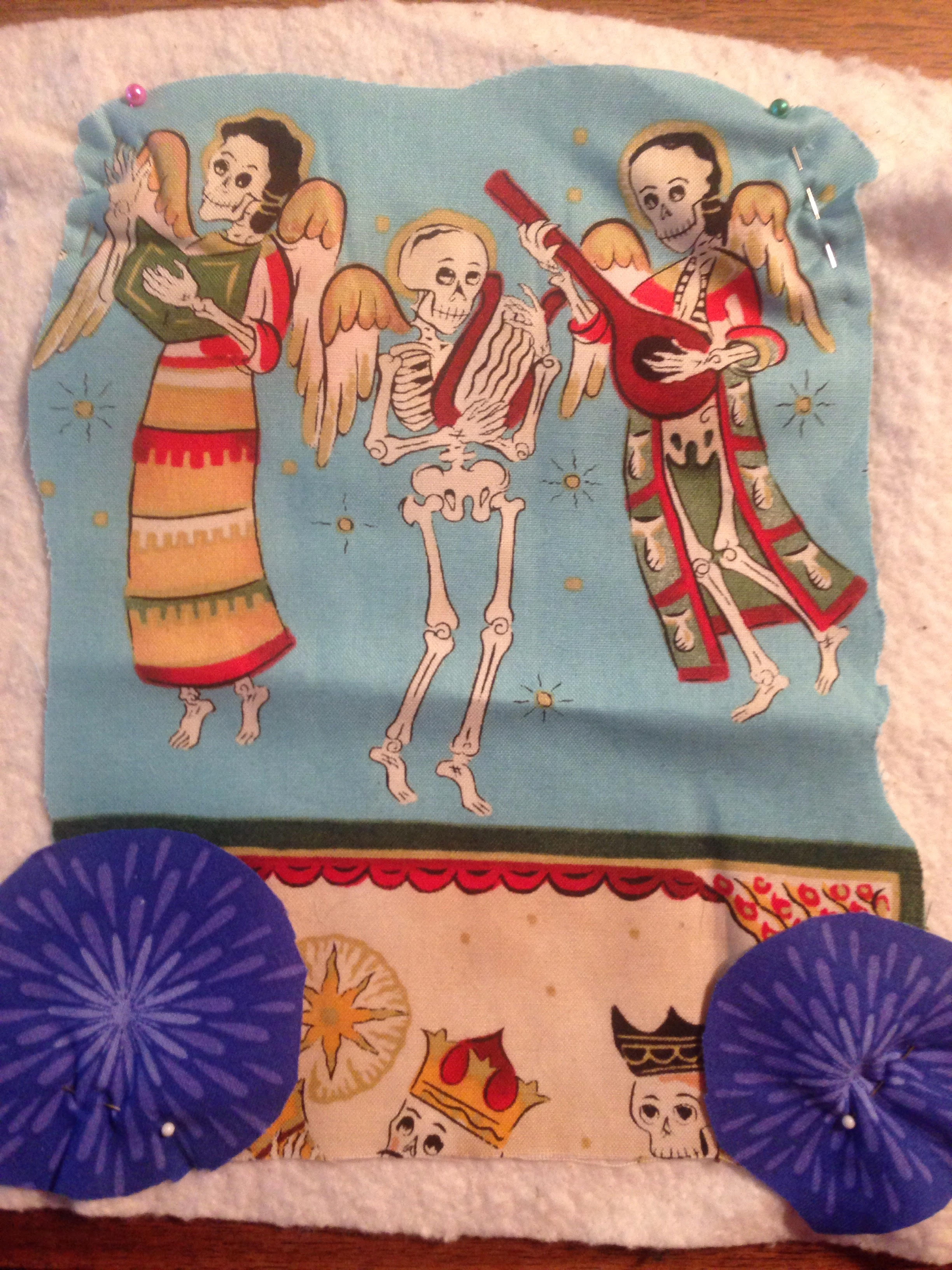 Small piece of fabric illustrating skull figures as angels playing musical instruments