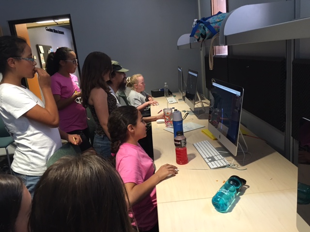 A group of campers teach coach Dylan how to play an online game.