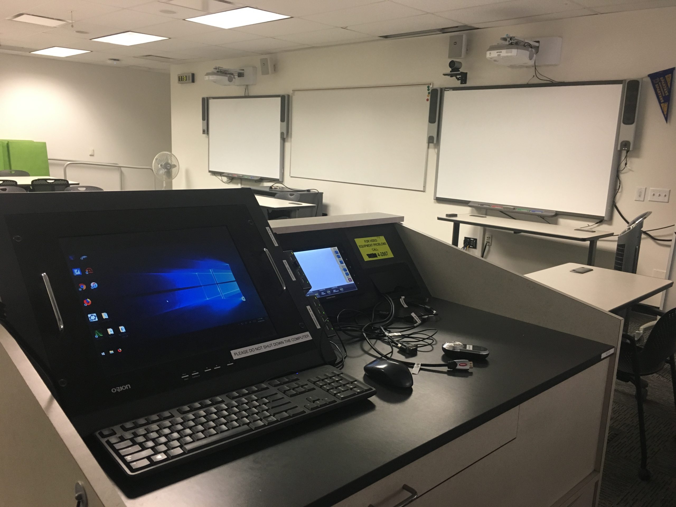 The inside of a Next Generation classroom, featuring a computer, tablet, projection screen, and two smart boards.