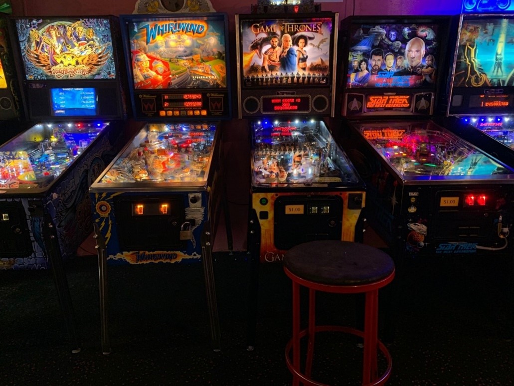 A series of pinball machines lit up in a dark arcade