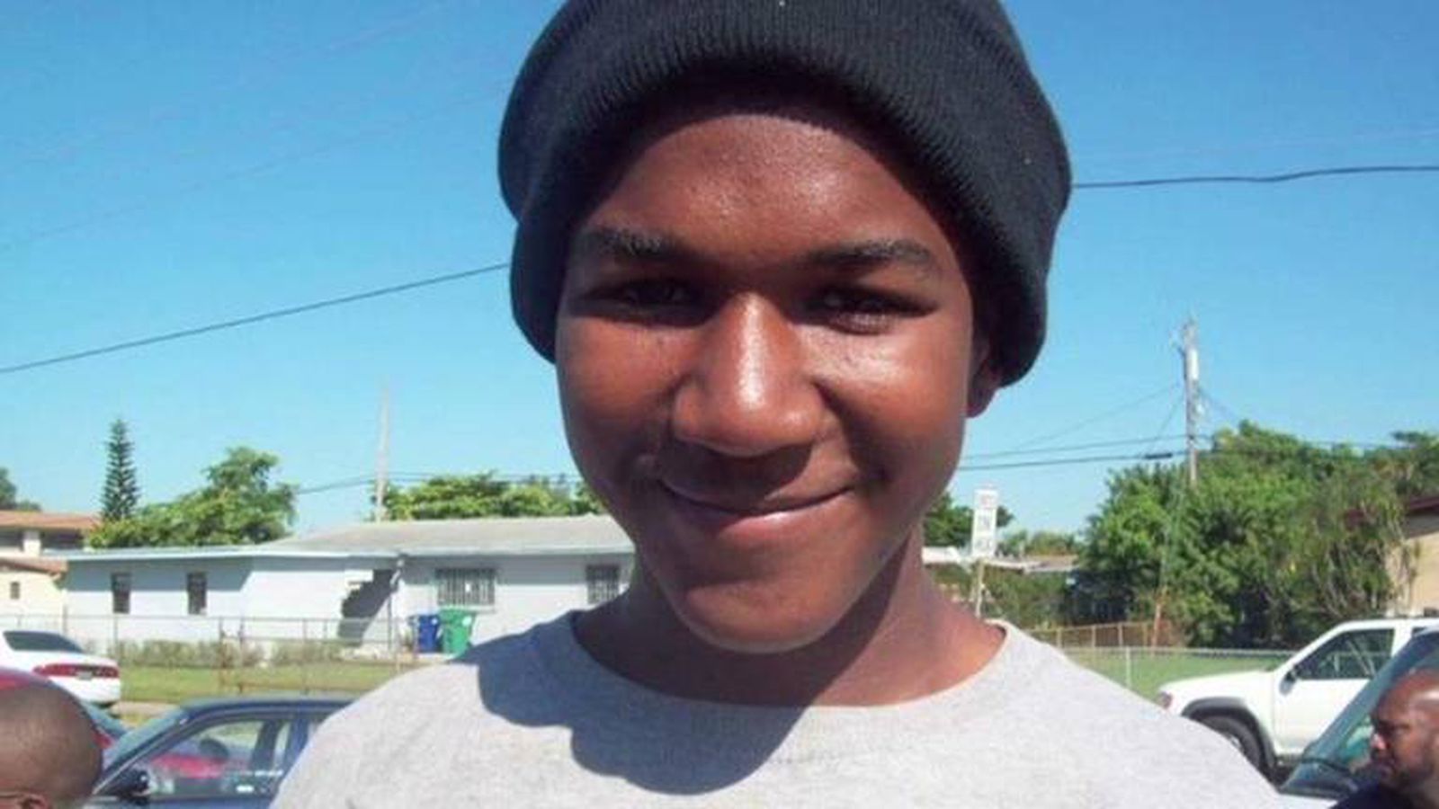 Trayvon Martin: young, Black man with gray t-shirt and black hat in front of a blue sky.