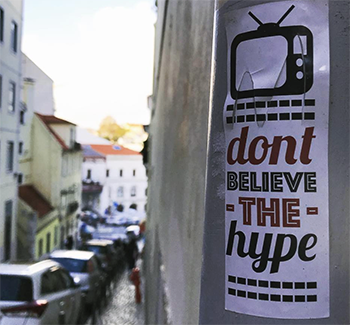 Sticker on lamppost on Lisbon street: an image of TV with the words, 'Don't Believe the Hype'