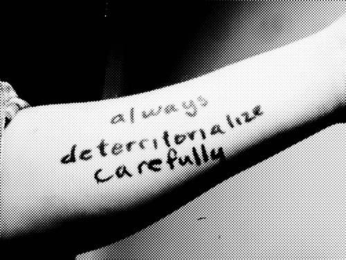 Black and white digitally modified photo of an arm with the words "always deterritorialize carefully" written across it. 